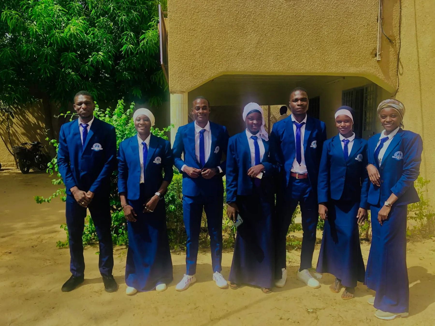 Sept étudiants du C.I.P.E.S.G. en uniforme bleu et cravate violette, devant un bâtiment du campus à Niamey